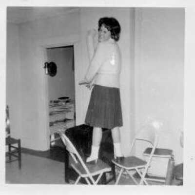 Peggy Handley Fitzgerald, class of 1963, standing on two chairs grinning.