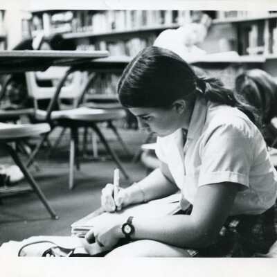 Girl writing and sitting on the floor in the library.