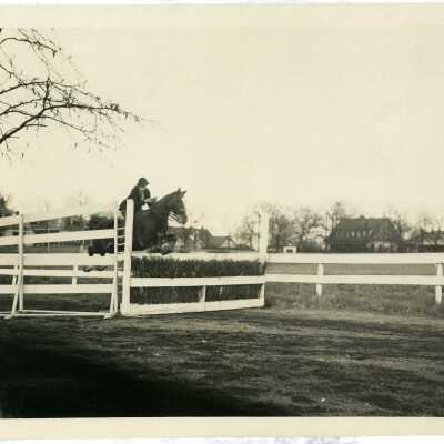 Photo of rider on a horse jumping over a fence/hedge.