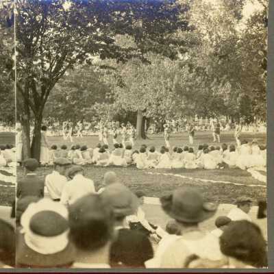 Belmont College for Young Women, circa 1910, women in gray clothing perform on lawn, while women in white are seated and onlooking with other spectators.