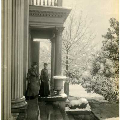 2 women standing outside of a building on a snowy day.