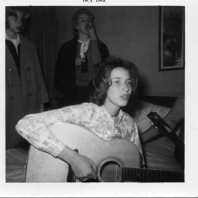 Student sitting on bed playing guitar in 1962.