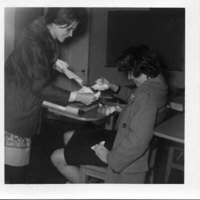 Student helping another student clean up a spill at her desk in 1963.
