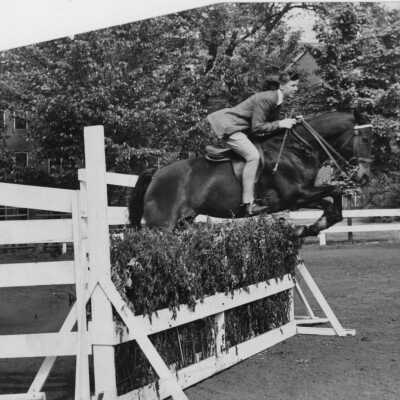 Woman riding horse jumping over fence/hedge (date unknown)