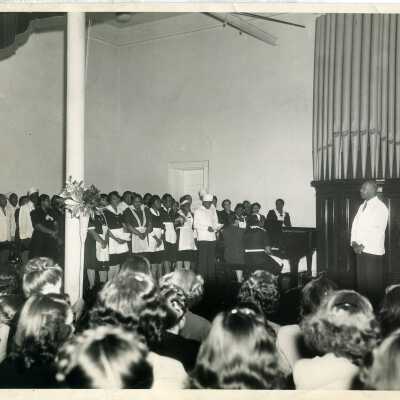 Photo from 1947 Milestones, photo shows audience of women listening to a group of African-American men and women singing.
