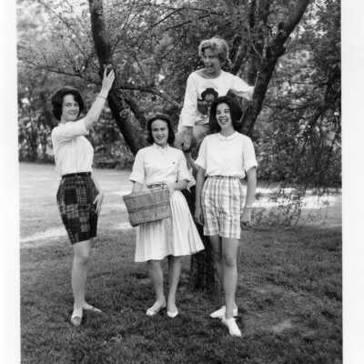4 Students by a tree in casual attire. One student is holding a basket.