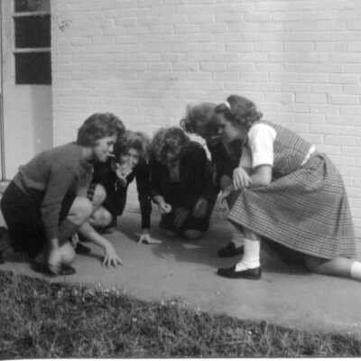 Students gathered on the sidewalk looking down at something. Circa 1960's.