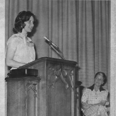 Student at podium in the auditorium during assembly. Idanelle McMurry in the background.
