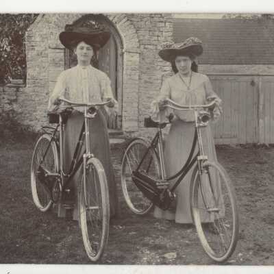 Postcard - Two women in hats with bikes