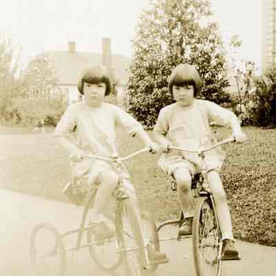 Unknown Young Girls Riding Tricycles on Sidewalk