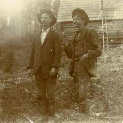 Unknown Men Standing by a Log House