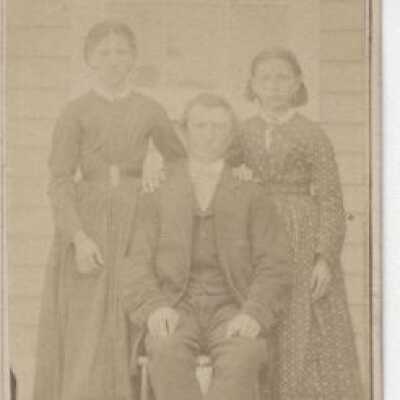 Photograph of Two Unknown women and man sitting in front of house