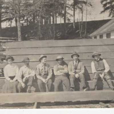 Five men and one woman sitting at a wooden wall