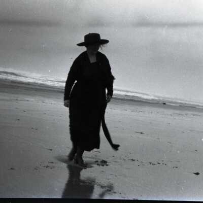 Woman in Hat Walking in Surf at Beach.