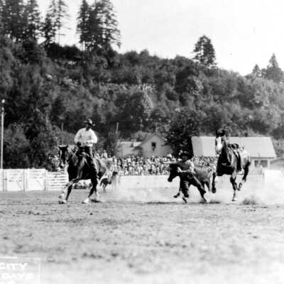 Oregon City Frontier Days - Kelly Field - Horses, bull, riders in arena.