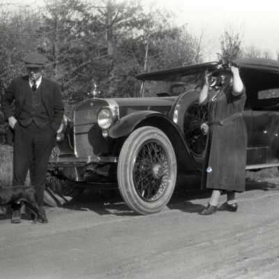 Man, Woman and Dog in Front of Car.