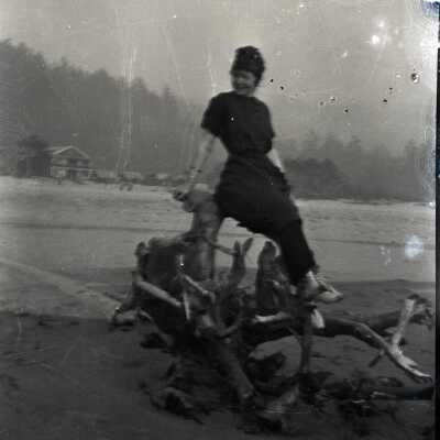 Woman Seated on Driftwood at Beach.