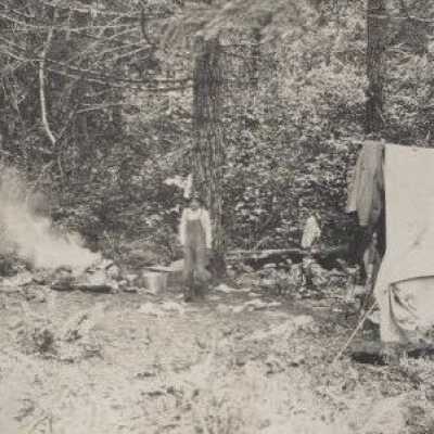 Campsite unknown location with man in overalls next to campfire - Print, photographic