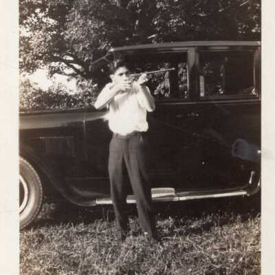 Man Holding Gun in Front of Automobile