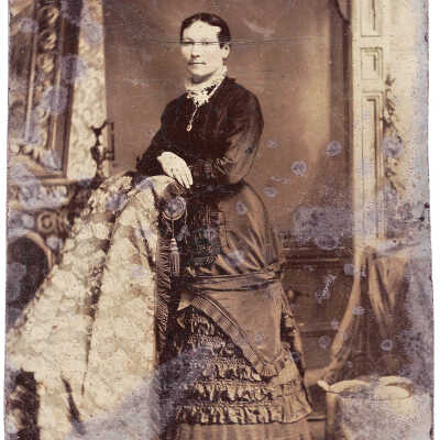 A tintype of a woman in a detailed gown.