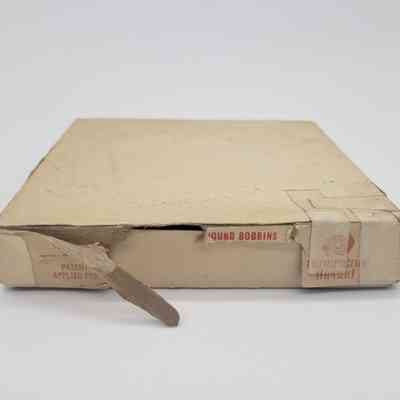 The image shows a worn, taped cardboard box marked "PATENT APPLIED FOR," containing wound bobbins.