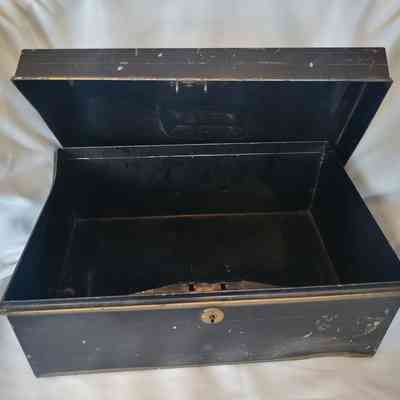 A black metal box with scratches is open, displaying its empty interior on a white fabric.