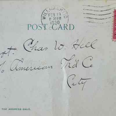 The address side of the postcard with a handwritten address. A red stamp is adhered to the top right corner with a stamped postmark over it. The card is stained in various places.