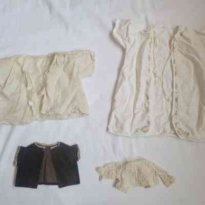 The image shows four vintage doll-sized garments on a white surface, including delicate blouses and a small jacket.