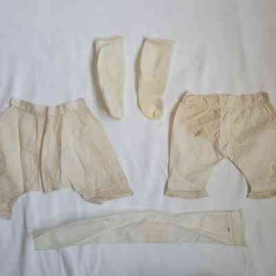 The image displays vintage doll’s clothing, including socks and undergarments, laid out on a white surface