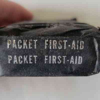 The image shows a black packet labeled "PACKET FIRST-AID" in white text twice.
