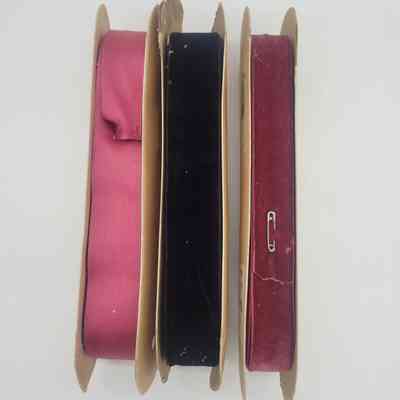 Three spools of fabric ribbon in pink, black, and red are neatly arranged.