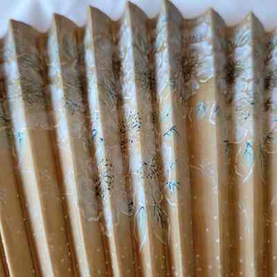 The image shows a close-up of a folded paper fan, adorned with intricate floral patterns in subtle colors