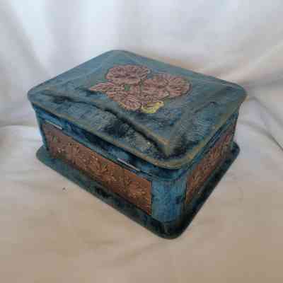 The image shows a vintage blue fabric box with floral patterns and intricate copper embellishments on its sides.