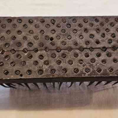 Hetchel, Bottom View: The image shows an antique hetchel, featuring a rectangular wooden base with a well-worn appearance, indicative of frequent use over time, and is topped with a metal sheet featuring numerous embedded, evenly spaced, small diamond-shaped protrusions designed to effectively work flax or other fibers; the contrasting materials and textures highlight the functional design, with two large holes on either side of the wooden structure likely used for mounting or securing purposes, and a piece of string looped through one of the holes, demonstrating a blend of both rustic charm and utilitarian craftsmanship, while the overall appearance suggests heavy historical use in textile preparation processes.