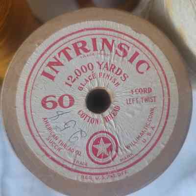 The image shows a wooden spool labeled "INTRINSIC," holding 12,000 yards of glace finish cotton thread.