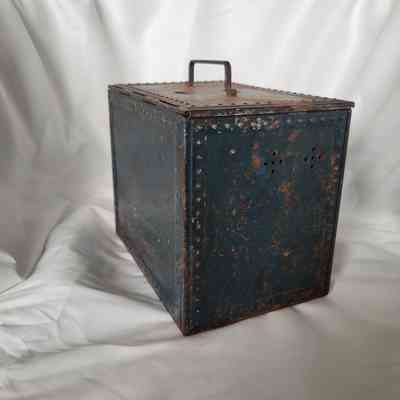 A blue, rusted metal box with a handle sits on a white, fabric-draped surface