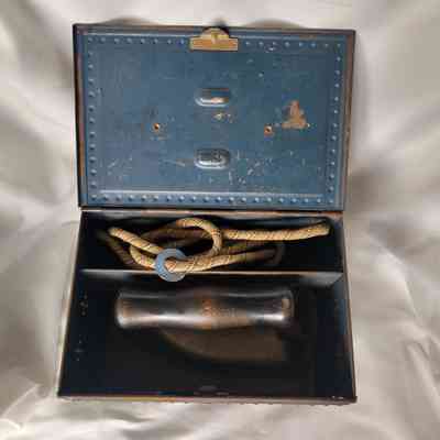 An opened vintage metal box contains a coiled cord and a handheld iron inside.