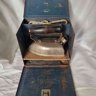 A vintage metal iron encased in a rusty blue box with a wooden handle.