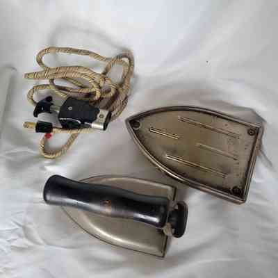 A vintage iron disassembled on white fabric, showing a cord and iron base.