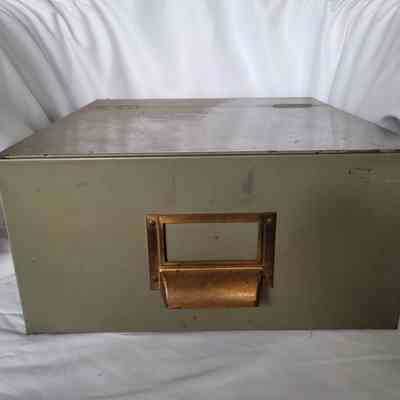 The image shows an old metal filing box with a vintage brass handle, set against a white fabric backdrop