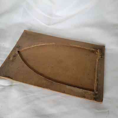 A worn, rectangular cardboard object lies on a white fabric, featuring carved sectional details.