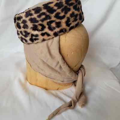 A mannequin head displays a leopard-print hat wrapped in beige fabric with a tied end.