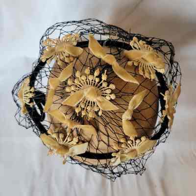 A decorative hat with yellow floral designs is encased in intricate black lace on top of a beige surface