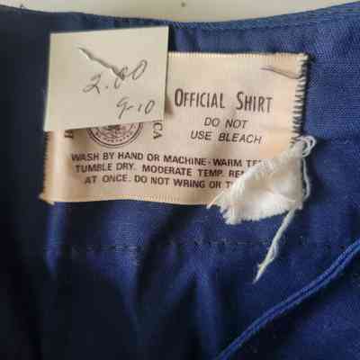 A clothing label on a blue shirt shows care instructions and a handwritten price tag attached.