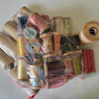 Two overlapping ziplock bags on a white background containing different colored thread on spools, as well as a large spool standing on end that reads The American Thread Co. Cushion Wind.