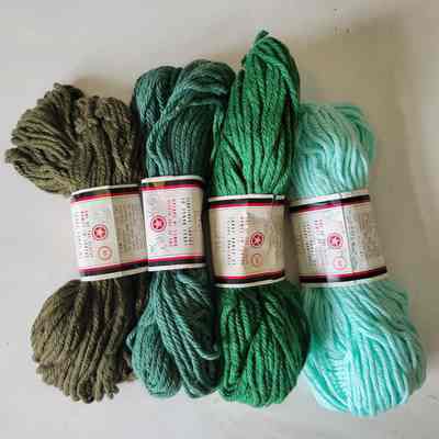 Four skeins of yarn on a white background. The yarns are each a difference shade of green and the white, red, and black labels feature a red star in circle logo.