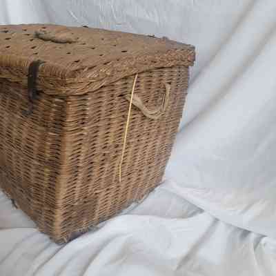 A large, woven wicker basket with handles sits on a white fabric background