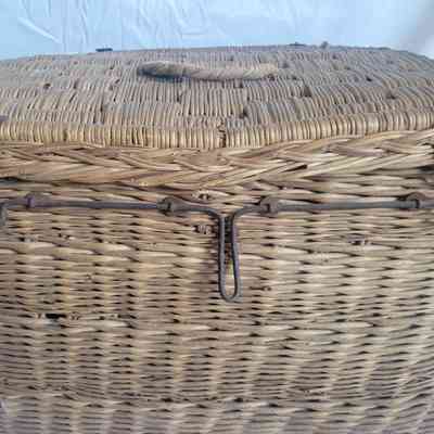 The image showcases a large woven wicker basket with a latch and metal handles against a white background.