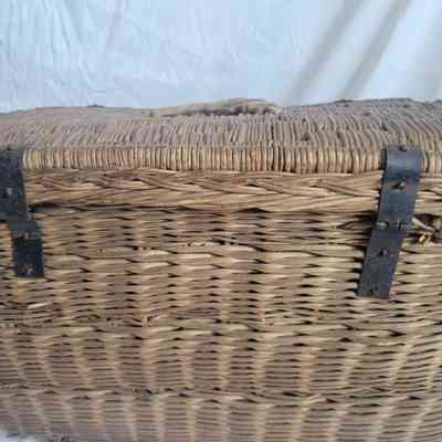 A woven wicker basket with metal clasps and a lid sits against a plain background.