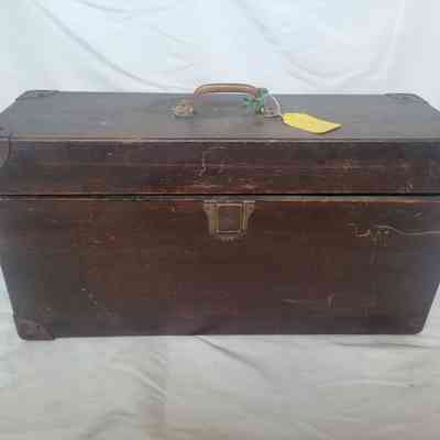 A vintage wooden trunk with metal reinforcements and a metal handle sits on a white surface.